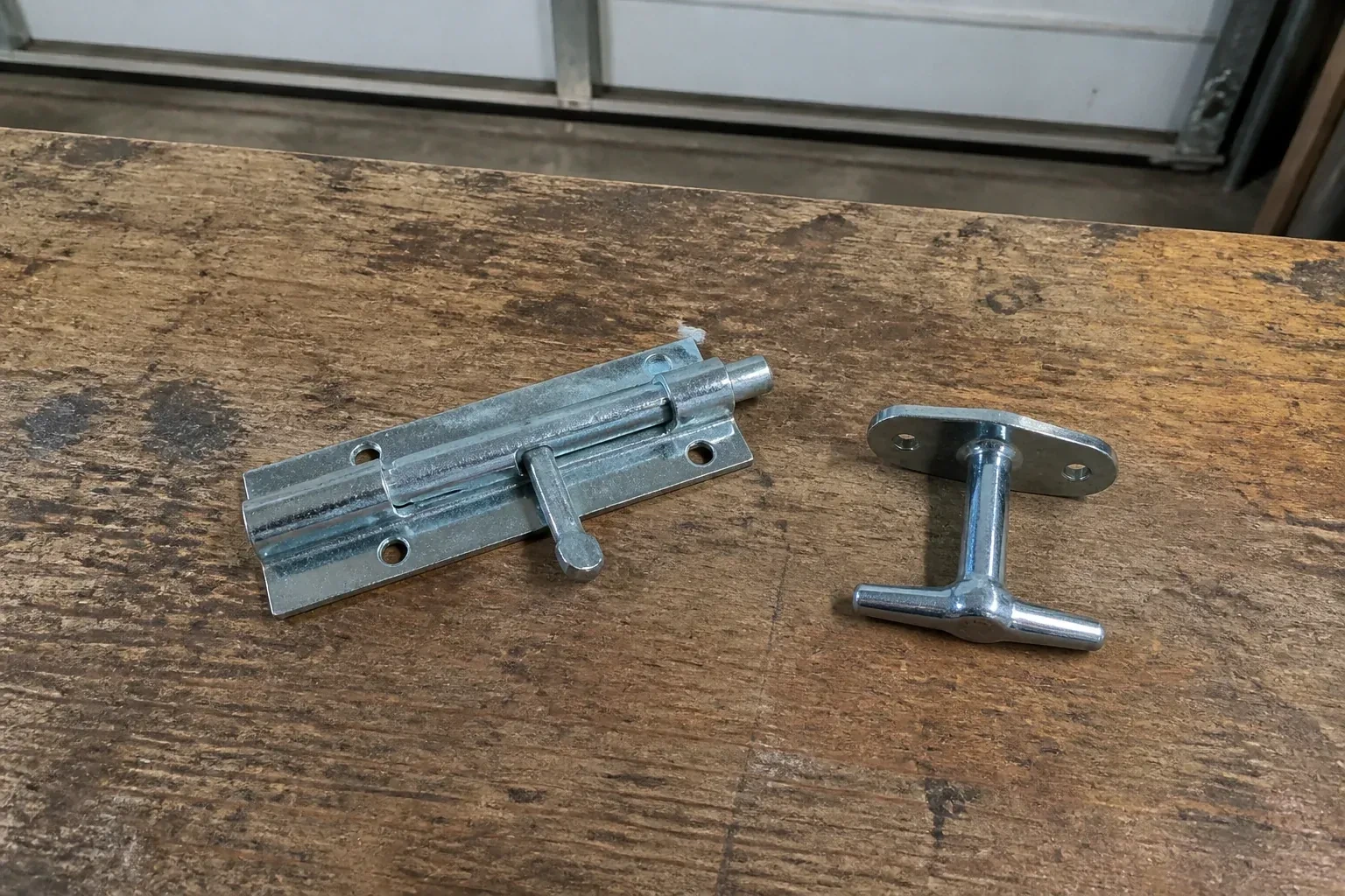 Detached slide bolt and T-handle on a wooden garage workbench. — Garage Door Manual Lock Repair, Hamilton