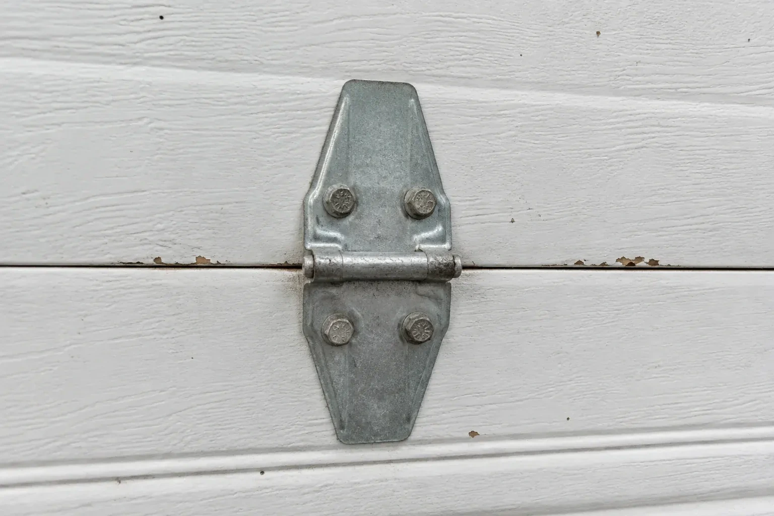 Metal center hinge across a seam in a white sectional garage door. — Garage Door Hinge Replacement, Hamilton